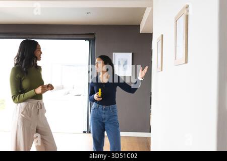 Positioning wooden frames Diverse female friends standing at door in home, with yellow laser meter Stock Photo