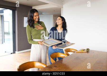 Holding frames, diverse friends measuring wall space in dining area, with tape measure and level Stock Photo