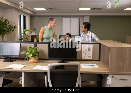 Collaborating Diverse coworkers discussing charts at desk in office, with computer monitors Stock Photo
