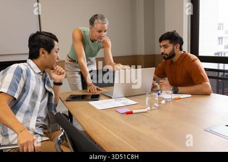 Diverse coworkers collaborating around laptop in conference room, with printed charts Stock Photo