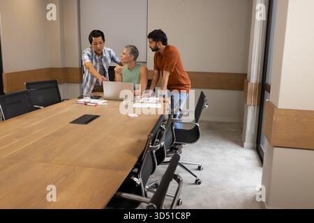 Discussing diverse coworkers collaborating around laptop, printed charts and pens in meeting room Stock Photo