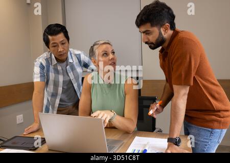 Collaborating diverse coworkers reviewing charts on wooden table in office, with laptop, tablet Stock Photo