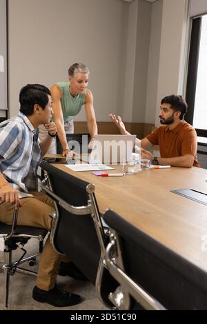 Discussing Diverse coworkers leaning over table in conference room, with open laptop and charts Stock Photo
