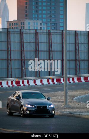 Dubai, UAE - July 13, 2024: A gray Lexus IS sedan with illuminated headlights driving on a curved city road, backed by modern skyscrapers and construc Stock Photo