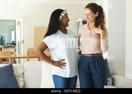 Talking Diverse female friends standing in open-plan living room, with white sofa and dining table Stock Photo