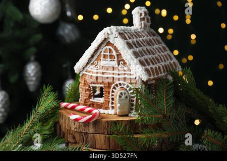 Gingerbread house, fir branches and candy cane against black background with blurred lights, closeup. Christmas treat Stock Photo