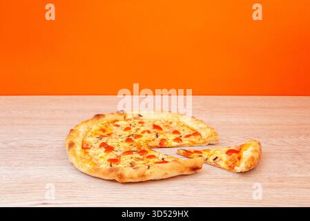 Partly eaten pizza with one missing slice on wooden table and orange background, symbolizing sharing, appetite, and homemade fast food Stock Photo
