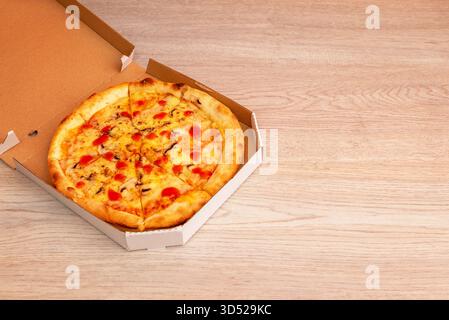 Pizza with melted cheese and tomato sauce in open cardboard box on wooden surface, perfect for takeaway or delivery service advertising Stock Photo