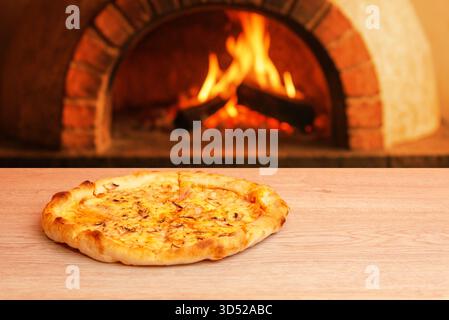 Pizza on wooden table with traditional brick oven and visible flames in background, warm and rustic atmosphere Stock Photo