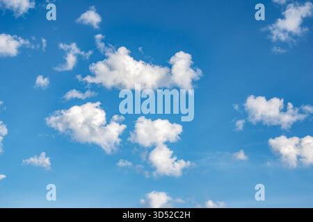 Fluffy cumulus clouds float in a vibrant blue sky under bright daylight conditions , selective focus Stock Photo