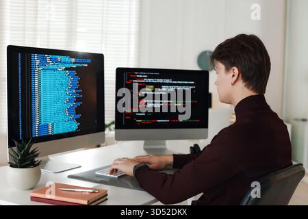 Programmer working on computer with dual monitors at white table in office Stock Photo