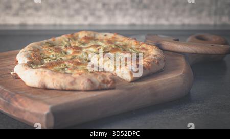 Crispy yet fluffy homemade pizza with melted cheese and greens resting on a wooden cutting board Stock Photo