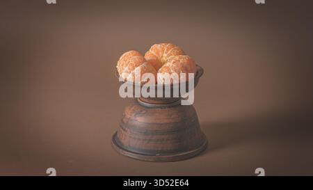 Bright peeled mandarins placed in a ceramic bowl on a table, simple rustic food still life Stock Photo