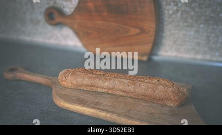 Long dark brown baguette on a rustic wooden board placed on a table, top-down shot for bakery and food advertising use Stock Photo