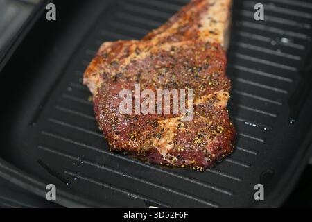 A close-up, high-resolution image of a raw tomahawk rib-eye steak cooking on a hot cast-iron grill pan. Stock Photo