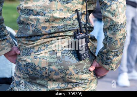 A military man is standing on the street in a camouflage uniform and with a walkie-talkie on his belt Stock Photo