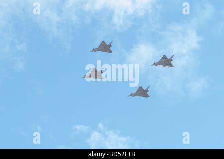 Four jet fighters are flying in a dense group in the blue sky under light clouds Stock Photo