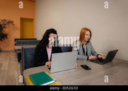 Two women working on laptops in a modern office, collaborating at a bright, professional table Stock Photo