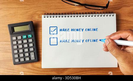 Hand checking Make Money Online on a checklist in a notebook with a calculator and glasses on a wooden desk. Stock Photo