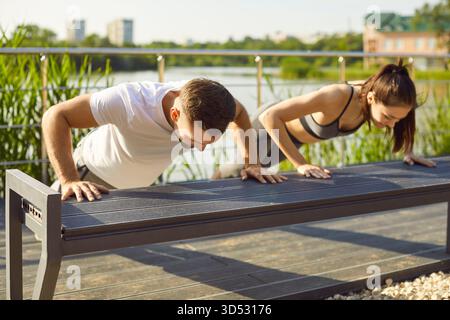 Sporty people actively exercising outdoors, doing push-ups leaning hands on bench Stock Photo