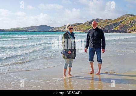 Happy smiling middle aged couple paddling at the waters edge on Oldshoremore Beach, Sutherland, Scottish Highlands, Scotland UK Stock Photo