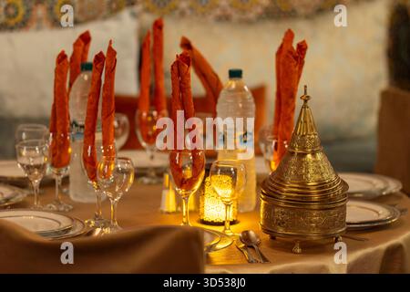 Elegant table setting in a traditional Moroccan restaurant with warm lighting. Arabian theme dinner table set up, moroccan style lidded container. Stock Photo