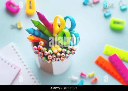 Colored pencils, scissors, notebook, ruler, pen, eraser, sharpener and more in glass. School and office stationery on light blue background. Concept back to school. Top view. Stock Photo