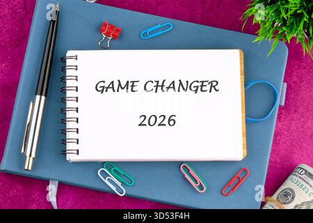 A planner sits on a desk with a note saying GAME CHANGER 2026. A pen, paper clips, money, and green plant are displayed, hinting at strategic planning Stock Photo