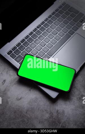 Smartphone laying on laptop keyboard with green screen for mockup. Mobile phone template. Stock Photo