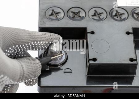 A gloved hand carefully measures the negative terminal of a black car battery with a black multimeter probe. The focus is on safety, precision, and pr Stock Photo