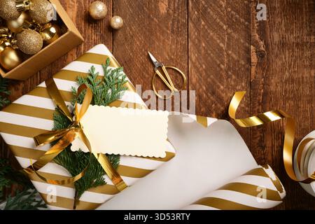 Christmas golden and white gift box with blank rectangular tag on wooden background. Copy space Stock Photo