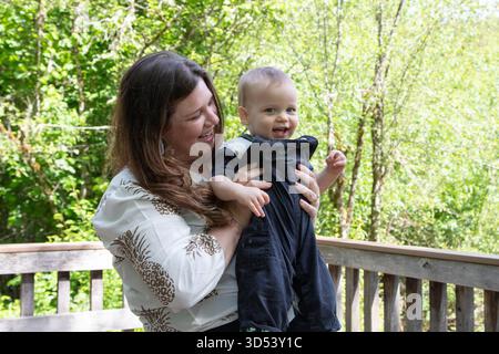 Smiling woman standing on a patio holding her baby son Stock Photo