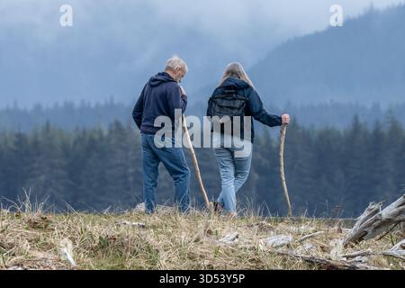 Rear view of a mature man and woman standing side by side in the countryside with walking sticks, British Columbia, Canada Stock Photo