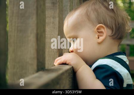 Side view of a boy standing on a terrace looking through a fence in summer, Florida, USA Stock Photo