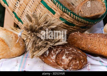 Close-up of assorted loaves of bread on a table with ears of wheat and basket at a street market Stock Photo