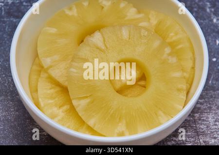 Sliced ​​pineapple, canned preserve. Close-up photograph with copy space on a table against a rustic background. Stock Photo