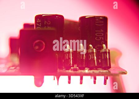 A close-up view of electronic components on a circuit board bathed in a vibrant pink light, highlighting small metallic connections and capacitors. Stock Photo