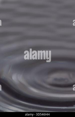 263.Macro photo of dark water surface showing ripple rings and soft wave patterns created by a droplet impact, with subtle reflections in shades of bl Stock Photo