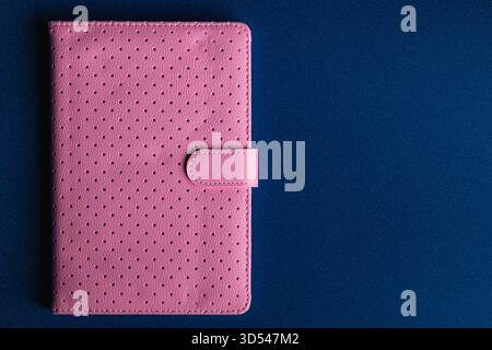 Overhead View of Closed Pink Perforated Notebook on Dark Blue Background Stock Photo