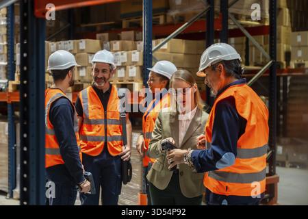 Warehouse manager and diverse workers standing together, reviewing operations and inventory data on a barcode scanner, ensuring efficient logistics an Stock Photo