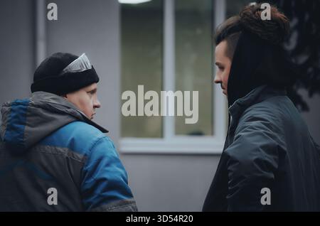 Two men in winter work clothes are discussing a project near a construction site. Cold weather and teamwork atmosphere of outdoor work. Stock Photo