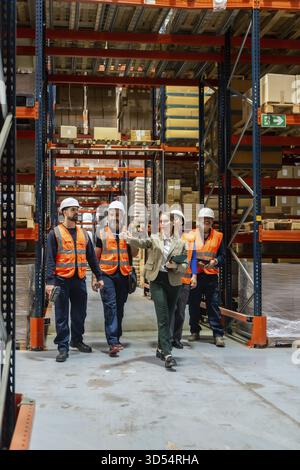 Diverse team of logistics professionals and warehouse workers discussing inventory management and safe operational procedures while walking through a Stock Photo
