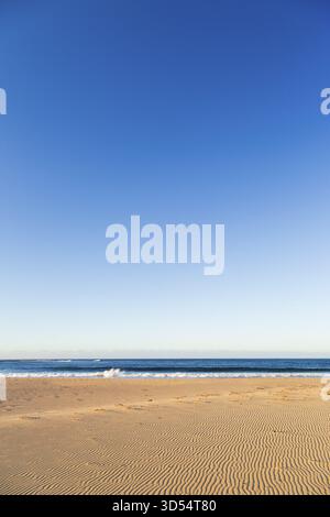 Vast sandy beach under a clear blue sky meeting the tranquil ocean, Margaret River Mouth beach, Margaret River, Western Australia Stock Photo