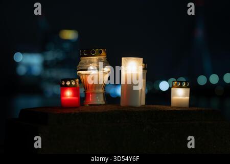 Warm candlelight placed on a riverside stone surface in Latvia, set against the out-of-focus cityscape and bridge structure, producing a serene nightt Stock Photo