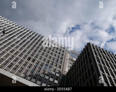 Low-angle view of modern office building facade with repetitive metal vertical fins and reflective glass windows under a cloudy sky. Ideal for archite Stock Photo
