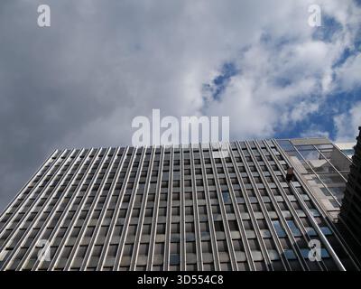Low-angle view of modern office building facade with repetitive metal vertical fins and reflective glass windows under a cloudy sky. Ideal for archite Stock Photo