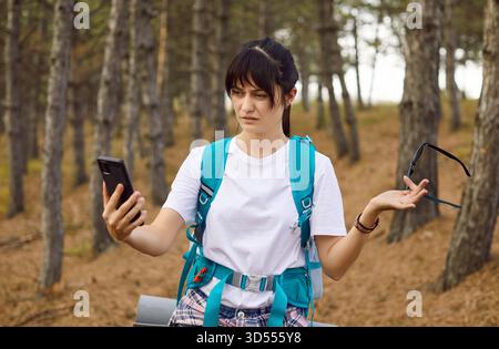 Female hiker frustrated by no connection, checking smartphone map in forest Stock Photo