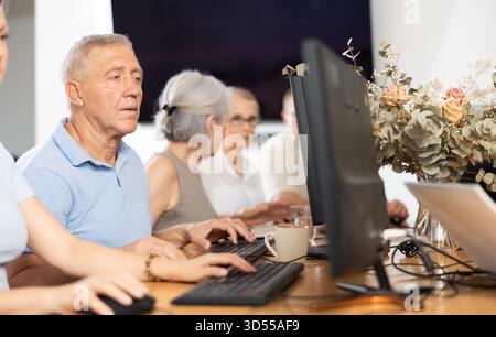 Concentrated elderly man immersed in using computer in library Stock Photo