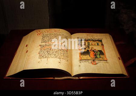 Open illuminated manuscript displayed under warm light in a museum. Stock Photo