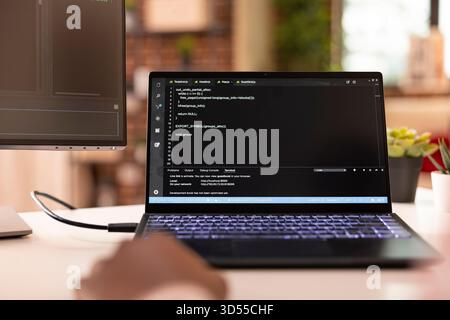 Closeup of laptop displaying code as african american developer troubleshoots app project from home. Black tech freelancer writing and debugging software script in modern apartment. Stock Photo
